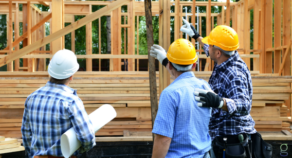 Three construction workers looking at and discussing a home under construction